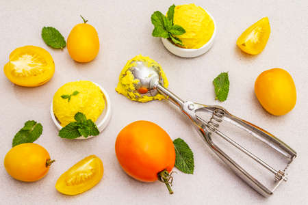 Yellow tomato ice cream, sorbet, gelato. Summer healthy refreshment dessert. Vegetarian (vegan) trendy food concept. With fresh vegetables and mint. Stone concrete backgroundの写真素材