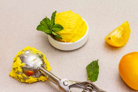 Yellow tomato ice cream, sorbet, gelato. Summer healthy refreshment dessert. Vegetarian (vegan) trendy food concept. With fresh vegetables and mint. Stone concrete background, close upの写真素材