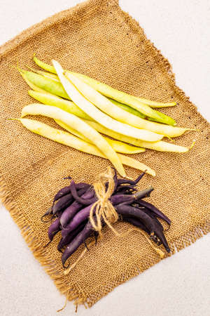 Assorted freshly colored beans in pods. Purple and yellow beans, on vintage sackcloth. Ingredient...