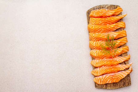 Slices of fresh salmon fish. Raw ingredient for cooking healthy seafood. Concept omega 3 containing food. Vintage wooden cutting board, stone concrete background, copy space, top viewの写真素材