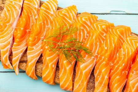Slices of fresh salmon fish. Raw ingredient for cooking healthy seafood. Concept omega 3 containing food. Vintage cutting board and wooden turquoise background, top view, close upの写真素材
