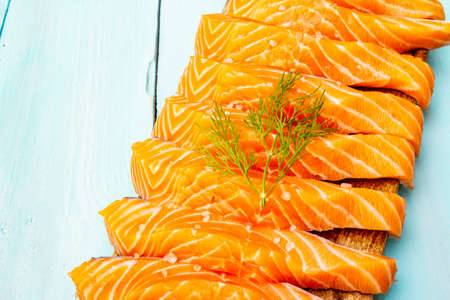 Slices of fresh salmon fish. Raw ingredient for cooking healthy seafood. Concept omega 3 containing food. Vintage cutting board and wooden turquoise background, copy space, close upの写真素材