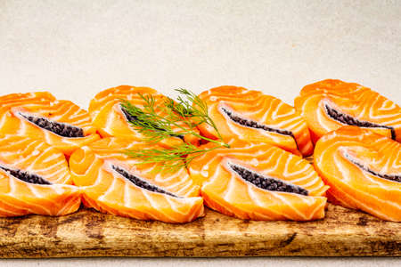Slices of fresh salmon fish in steak shape. Raw ingredient for cooking healthy seafood. Concept omega 3 containing food. Vintage wooden cutting board, stone backgroundの写真素材