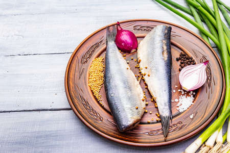 Traditional Norwegian slightly salted herring. Healthy seafood concept. Vegetarian ingredient with fresh onion, dry spice on ceramic plate. Rustic style, wooden boards background, copy spaceの写真素材