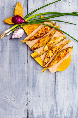 Fried smelt with fresh onions. Healthy seafood with the smell of cucumber, crispy breading. On a wooden board in the shape of a fish. Gray wooden boards background, copy space, top viewの写真素材