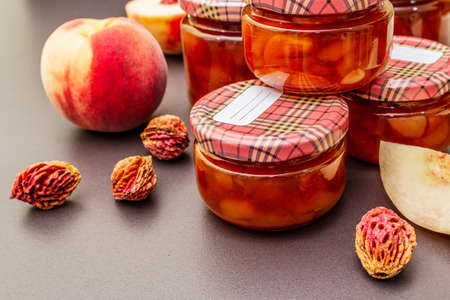 White peach jam, confiture, chutney in a glass jar. Homemade preservation concept. With fresh fruits, dry seeds on black stone concrete background, close upの写真素材