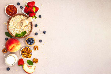 Cereal and various delicious ingredients for breakfast. Oat, blueberry, strawberry, walnuts, peach jam and mint. Ethnic ceramic bowl. Stone concrete background, copy space, top viewの写真素材