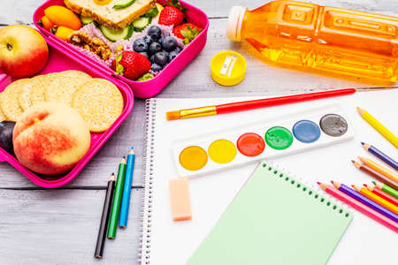 School lunch box with sandwich, fresh fruits, vegetables, cookies, juice and nuts. Healthy eating habits for kids. Back to school concept. With school supplies, wooden boards backgroundの写真素材