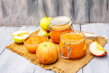 Apple jam, confiture, chutney in a glass jar. Homemade preservation concept. With fresh apples on vintage sackcloth, rustic spoon on gray wooden boards background, copy space, close upの写真素材