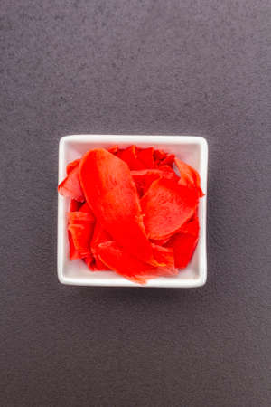Pickled sushi ginger slices in white bowl. Traditional oriental food supplement, on black stone background, copy space, top view, flat layの写真素材