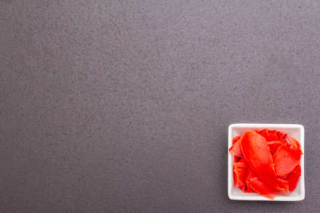 Pickled sushi ginger slices in white bowl. Traditional oriental food supplement, on black stone...