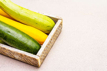 Assorted colorful zucchini in wooden box. Fresh vegetables for cooking. Harvest on stone background,...