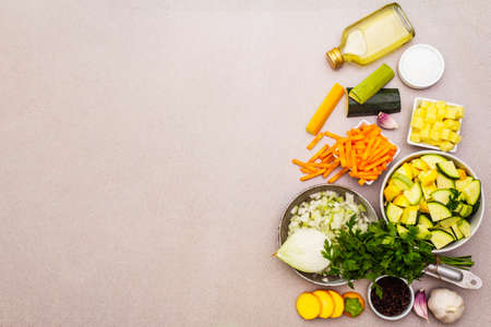 Set of fresh raw ground vegetables for cooking soup puree. Vintage pan with onion, salt, spices, parsley, olive oil. Healthy food concept on a stone background, copy space, top viewの写真素材