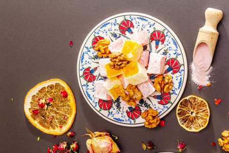 Eastern sweets. Traditional Turkish delight Rahat lukum with rose and citrus on ceramics with typical folk patterns. Fruit sugar, sumac in wooden shovels stone background copy space top viewの写真素材