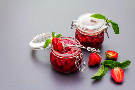 Strawberry jam in a glass jar. Homemade preservation concept. With fresh strawberries and mint, silver spoon on black stone backgroundの写真素材