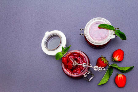 Strawberry jam in a glass jar. Homemade preservation concept. With fresh strawberries and mint, silver spoon on black stone background, top view, copy spaceの写真素材