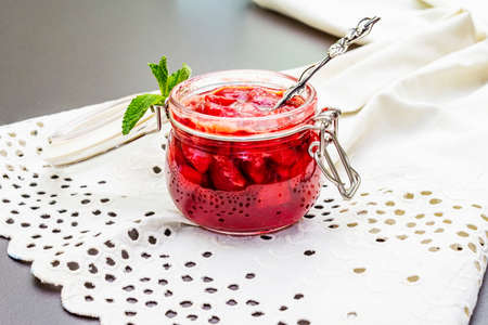 Strawberry jam in a glass jar. Homemade preservation concept. With fresh strawberries and mint, silver spoon on black stone background, vintage linen cloth, close upの写真素材