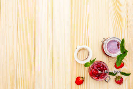 Strawberry jam in a glass jar. Homemade preservation concept. With fresh strawberries and mint, silver spoon on wooden background, top view, copy spaceの写真素材