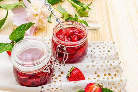 Strawberry jam in a glass jar. Homemade preservation concept. With fresh strawberries and mint, silver spoon, fresh peonies, vintage linen cloth on wooden background, close upの写真素材