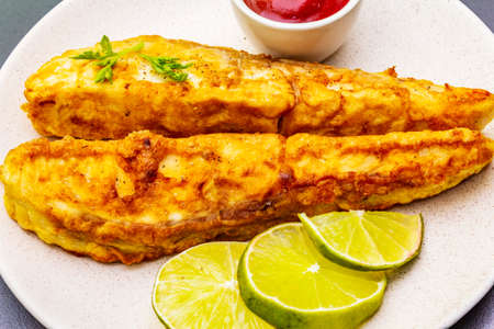 Grilled (fried) pollock in batter. On ceramic plate with lime, parsley and sauce. Cooking fresh fish, macroの写真素材