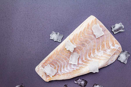 Frozen pollock fillet with pieces of ice. Concept of healthy seafood. Organic fish on a black stone background, copy space, top viewの写真素材