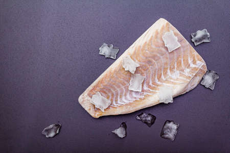 Frozen pollock fillet with pieces of ice. Concept of healthy seafood. Organic fish on a black stone background, copy space, top viewの写真素材