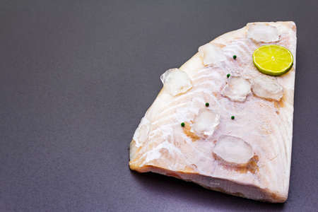 Frozen pollock fillet with pieces of ice. Concept of healthy seafood. Organic fish on a black stone background, close up, copy spaceの写真素材