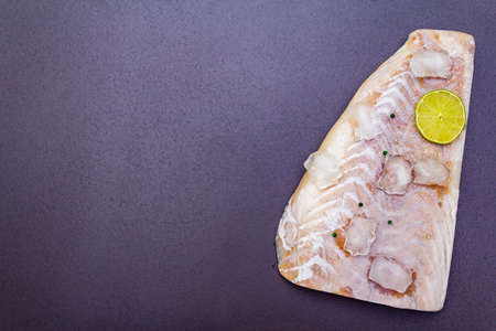 Frozen pollock fillet with pieces of ice. Concept of healthy seafood. Organic fish on a black stone background, close up, top view, copy spaceの写真素材