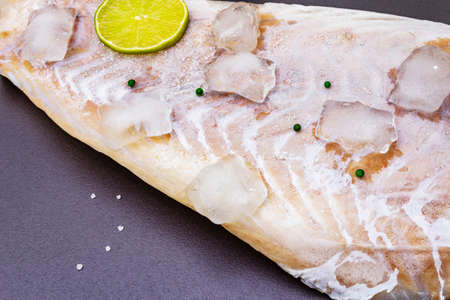 Frozen pollock fillet with pieces of ice. Concept of healthy seafood. Organic fish on a black stone...
