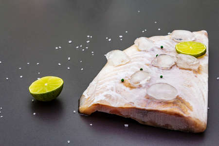 Frozen pollock fillet with pieces of ice. Concept of healthy seafood. Organic fish on a black stone background, close up, copy spaceの写真素材