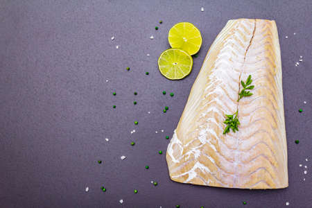 Fresh pollock fillet with lime, green pepper, salt and parsley. Concept of healthy seafood. Organic fish on a black stone background, copy space, top viewの写真素材