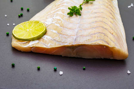 Fresh pollock fillet with lime, green pepper, salt and parsley. Concept of healthy seafood. Organic fish on a black stone background, close upの写真素材