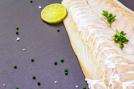 Fresh pollock fillet with lime, green pepper, salt and parsley. Concept of healthy seafood. Organic fish on a black stone background, copy space, close upの写真素材