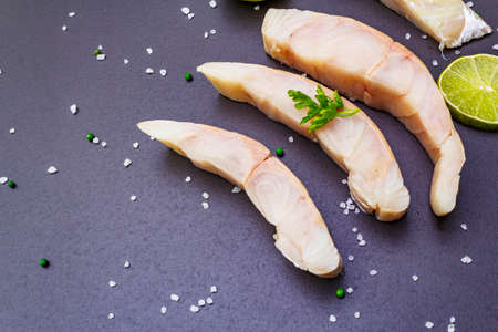 Fresh pollock pieces with lime, green pepper, salt and parsley. Concept of healthy seafood. Organic fish on a black stone background, copy spaceの写真素材