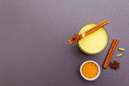 Golden turmeric milk. Cinnamon, cardamon, anise spices. Trendy healthy drink concept. In glass on stone background, top view, copy spaceの写真素材
