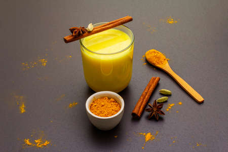 Golden turmeric milk. Cinnamon, cardamon, anise spices. Trendy healthy drink concept. In glass on stone background, close upの写真素材