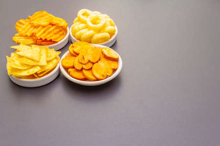Assorted salty spiced snacks. Chips, rings, nachos, crackers. In ceramic bowls on a stone background, copy spaceの写真素材