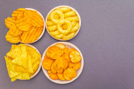 Assorted salty spiced snacks. Chips, rings, nachos, crackers. In ceramic bowls on a stone background, copy space, top viewの写真素材