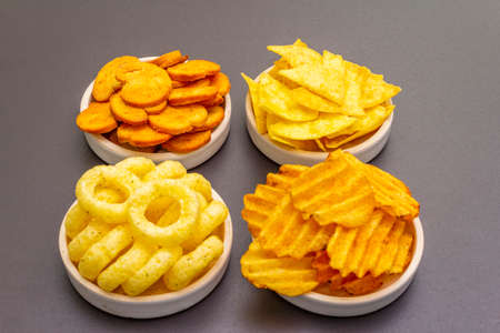 Assorted salty spiced snacks. Chips, rings, nachos, crackers. In ceramic bowls on a stone background, close upの写真素材