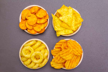 Assorted salty spiced snacks. Chips, rings, nachos, crackers. In ceramic bowls on a stone background, top view, close upの写真素材