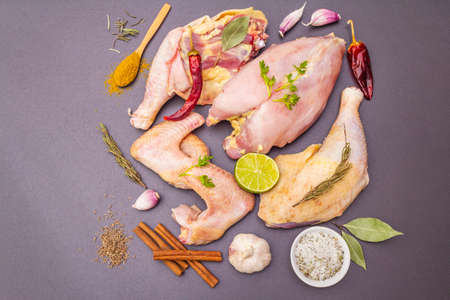 Fresh raw pieces of organic (bio) poultry chicken. Breast (fillet) on the bone, legs (thighs), wings. Spices and vegetables. Traditional Indian, Thai cooking concept. Stone background, top viewの写真素材