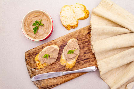 Chicken liver pate with butter. Crunchy baguette with flax and poppy seeds, fresh parsley. Concept of traditional french food. Vintage wooden board, linen napkin, on stone background, top viewの写真素材
