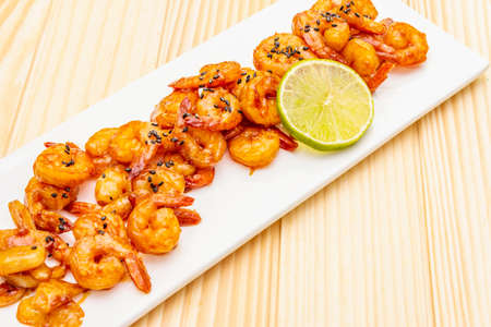 Fresh organic fried shrimp (prawns). Delicious seafood in teriyaki sauce with lime. On wooden boards background, close up.の写真素材