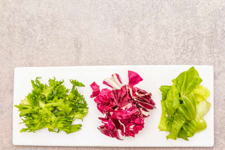 Vegan (vegetarian) healthy food concept. Fresh organic salad mix of radicchio, escarole endive and frize lettuce. On white ceramic plate on stone cooking background, copy space, top viewの写真素材