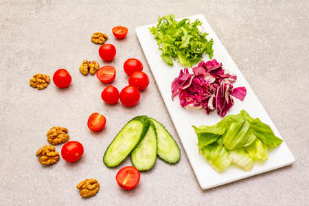 Vegan (vegetarian) healthy food concept ingredients. Fresh organic vegetables, walnuts and salad mix on stone cooking background, close upの写真素材