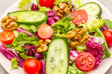 Vegan (vegetarian) healthy food concept ingredients. Fresh organic vegetables, walnuts and salad mix in ceramic plate on stone cooking background, macroの写真素材