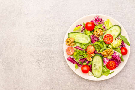 Vegan (vegetarian) healthy food concept ingredients. Fresh organic vegetables, walnuts and salad mix in ceramic plate on stone cooking background, copy space, top viewの写真素材