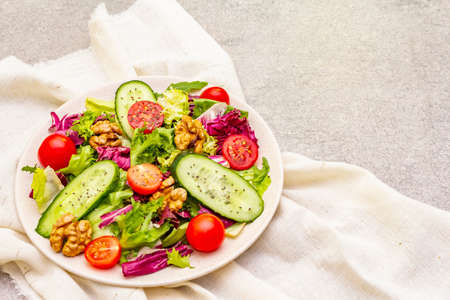 Vegan (vegetarian) healthy food concept ingredients. Fresh organic vegetables, walnuts and salad mix in ceramic plate on stone cooking background, copy spaceの写真素材