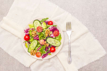 Vegan (vegetarian) healthy food concept ingredients. Fresh organic vegetables, walnuts and salad mix in ceramic plate on stone cooking background, copy space, top viewの写真素材