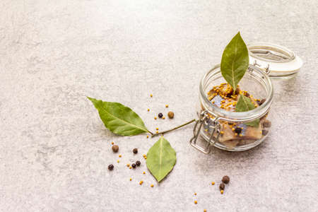 Slices of herring with spices in a glass jar. Mustard seeds, bay leaf, pepper mix. Healthy traditional food concept. Stone background, copy spaceの写真素材